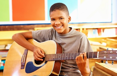 child with a smile holding a quitar